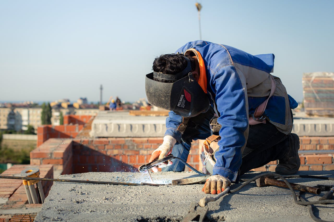 why-choose-us Focused welder in protective gear welding on a city rooftop construction site.
