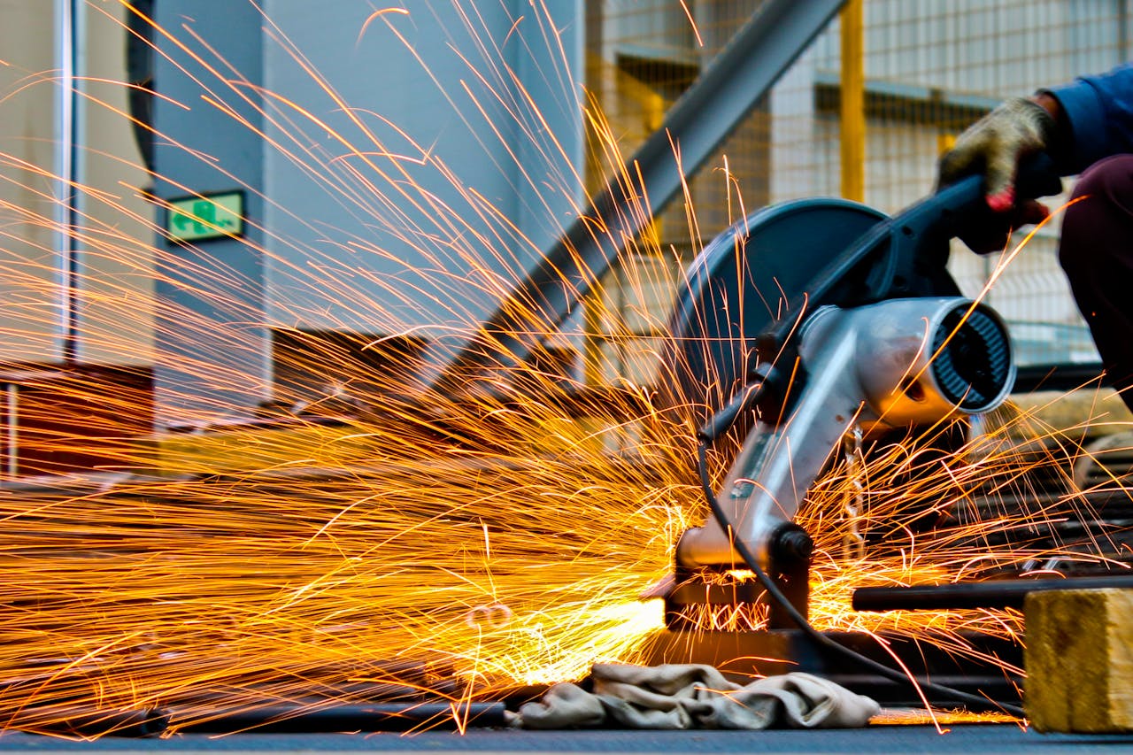 home-hero A worker operates a grinder cutting metal, creating a vibrant display of sparks in an industrial setting.